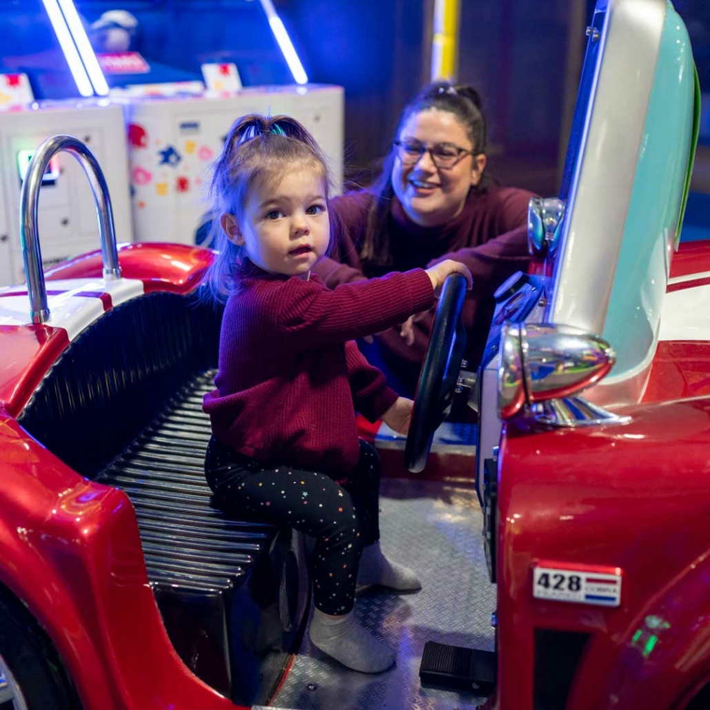 toddler riding a red kiddie ride with her mom smiling